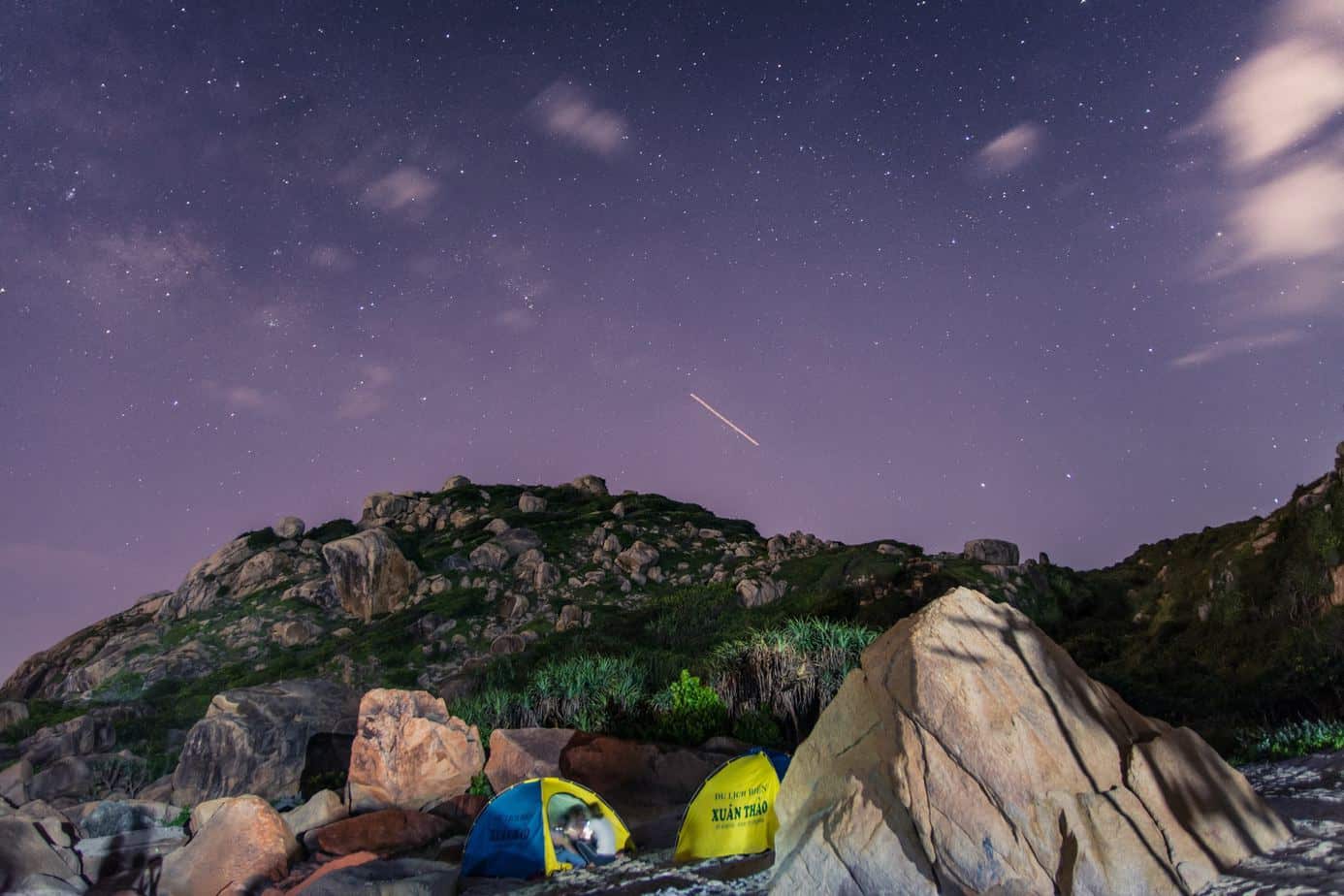 A tent surrounded by green rocks under a purple sky at night